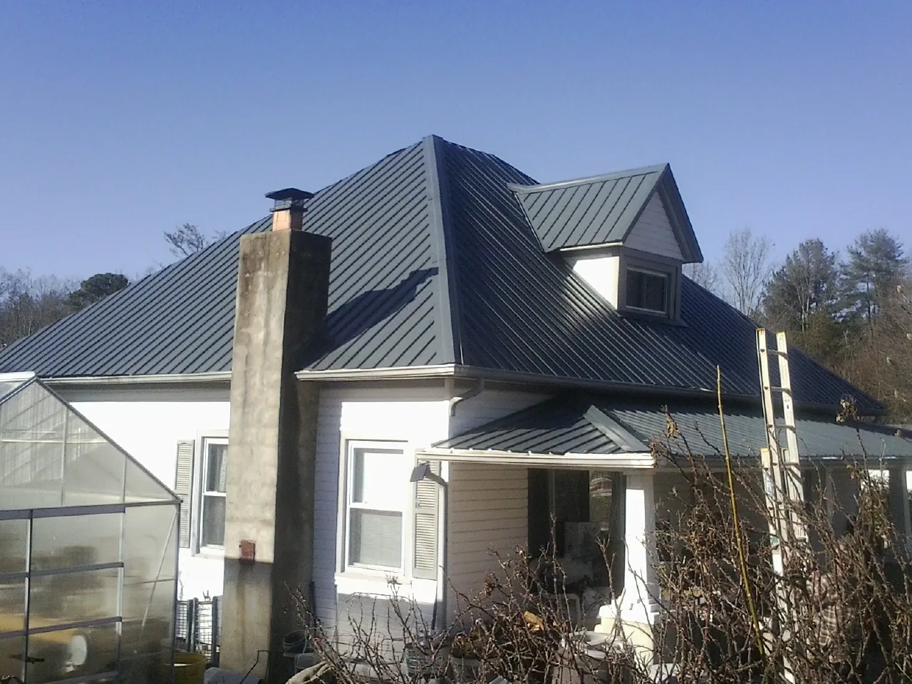 Dark blue standing seam metal roof on a white farmhouse with dormer — Slate & Tile Roof Repair by Roofing Brothers in Colton