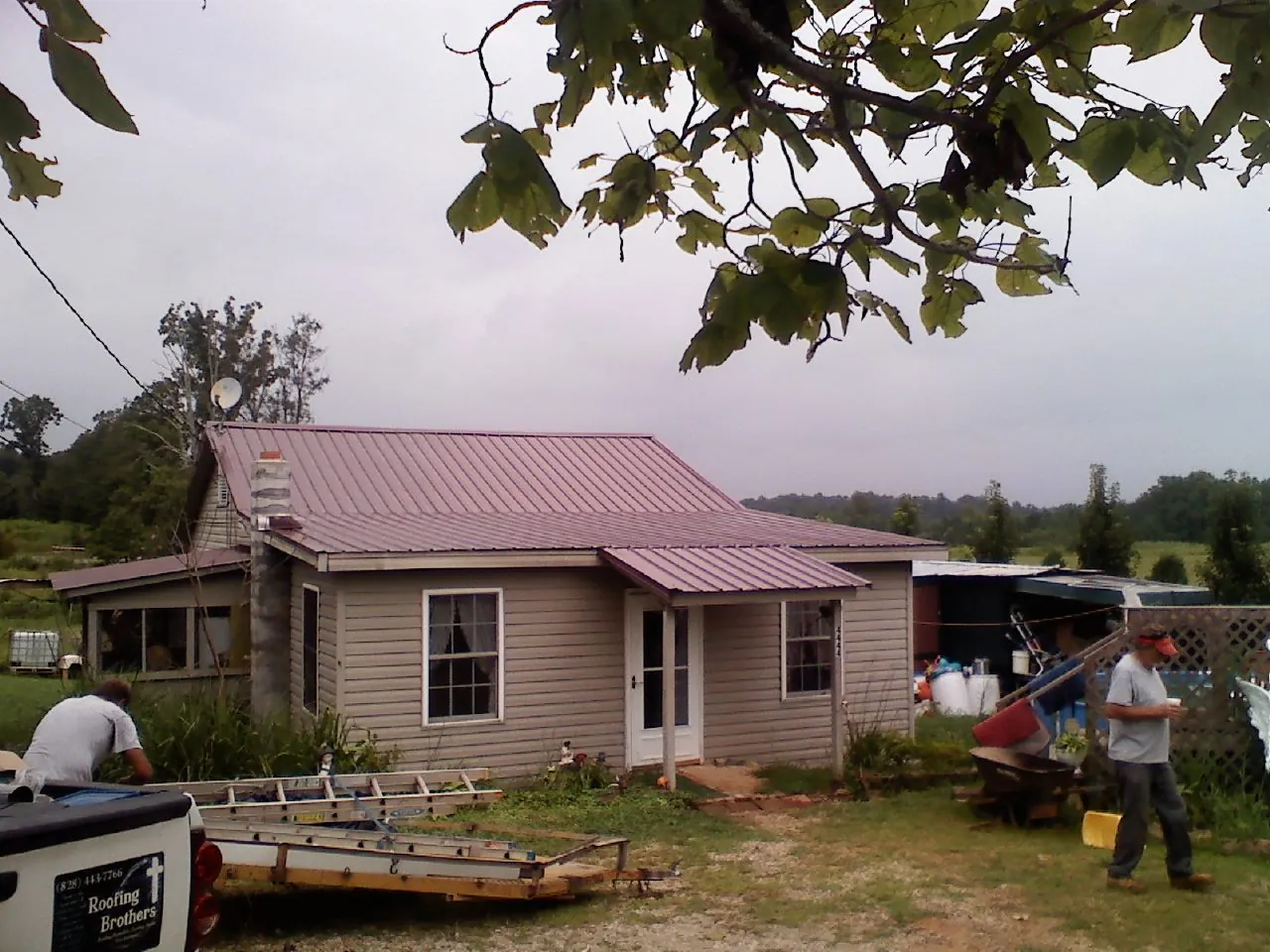 Crew finishing a mauve metal roof on a small farmhouse in Colton