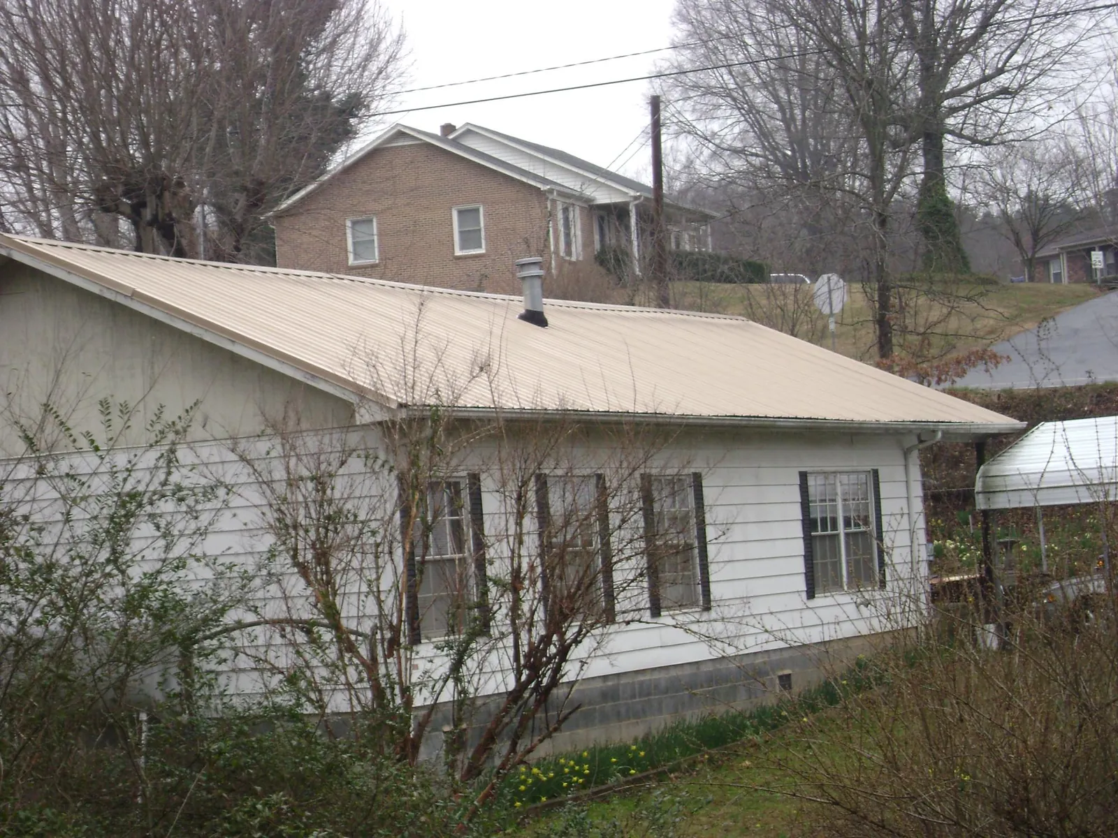 Tan metal roof on a white sided house set into a hillside — Commercial Roofing by Roofing Brothers in Colton